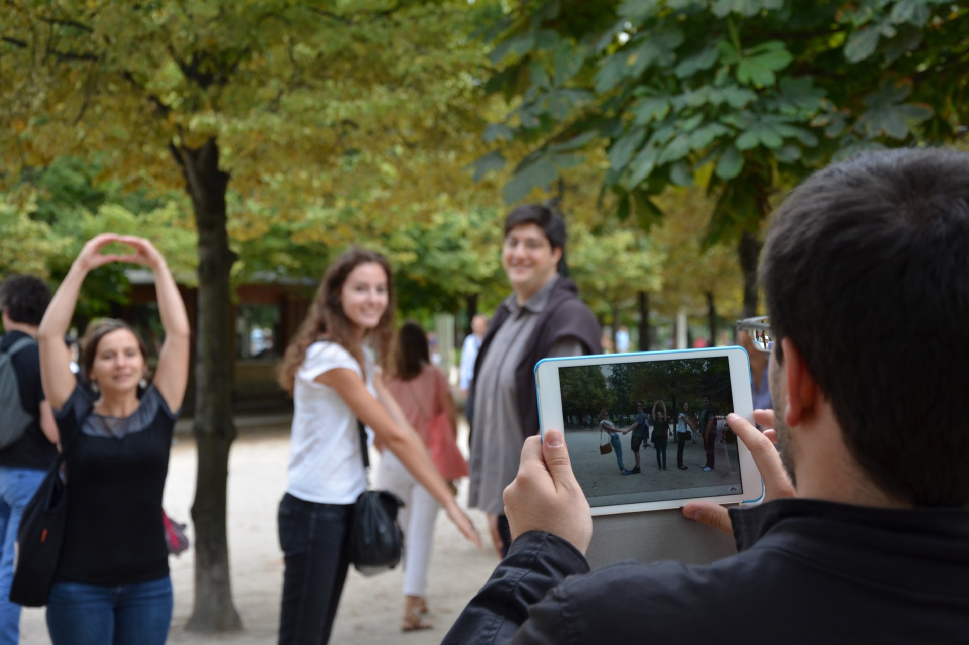 Dans un parc, un groupe pose pendant qu'une personne les photographie avec une tablette.